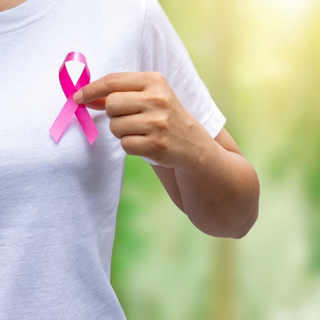 Woman in white tshirt holding pink breast cancer ribbon at her chest